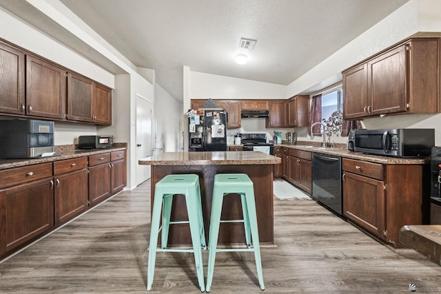 kitchen featuring a sink, light wood finished floors, lofted ceiling, visible vents, and black appliances