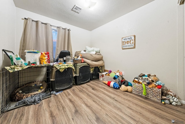 interior space with a textured ceiling, visible vents, wood finished floors, and lofted ceiling