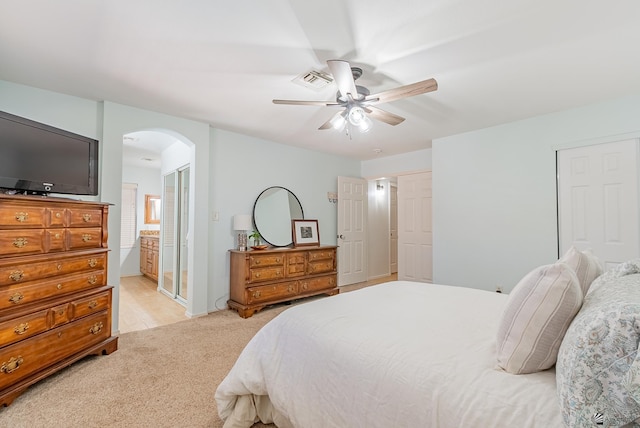 bedroom featuring arched walkways, a ceiling fan, light colored carpet, and ensuite bath