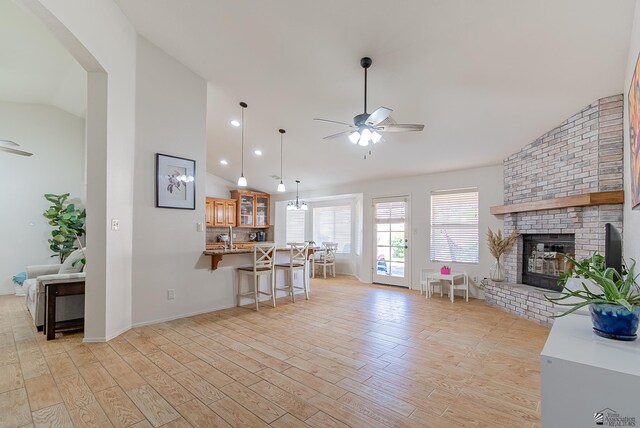 living area with a brick fireplace, a ceiling fan, vaulted ceiling, and light wood-style flooring