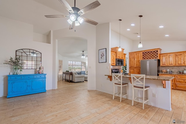 kitchen featuring decorative backsplash, ceiling fan, a kitchen bar, light stone counters, and stainless steel appliances