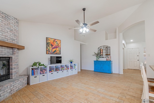 living room with ceiling fan, a brick fireplace, arched walkways, wood finished floors, and vaulted ceiling
