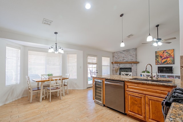kitchen with stainless steel dishwasher, a fireplace, brown cabinets, a sink, and beverage cooler