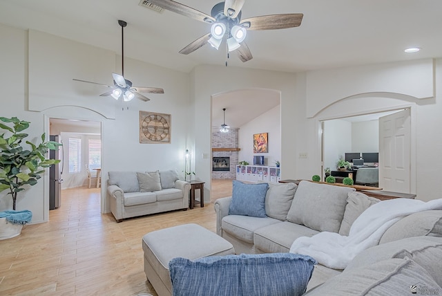 living area with ceiling fan, visible vents, arched walkways, a fireplace, and light wood-style flooring