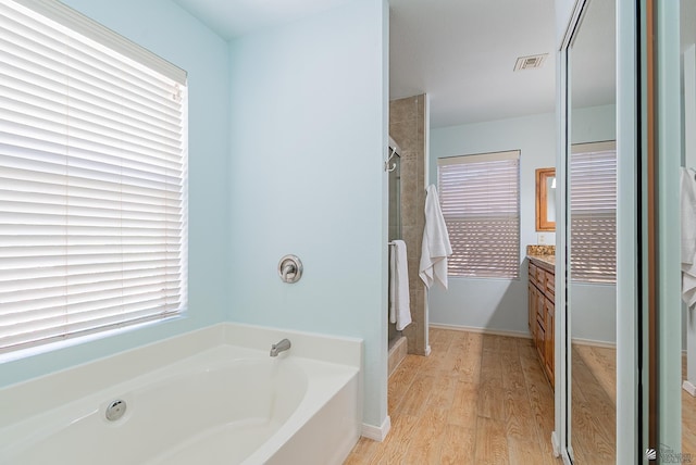 full bathroom with vanity, a garden tub, a stall shower, and wood finished floors