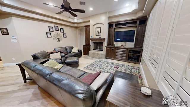 living area with a brick fireplace, a tray ceiling, visible vents, and ceiling fan