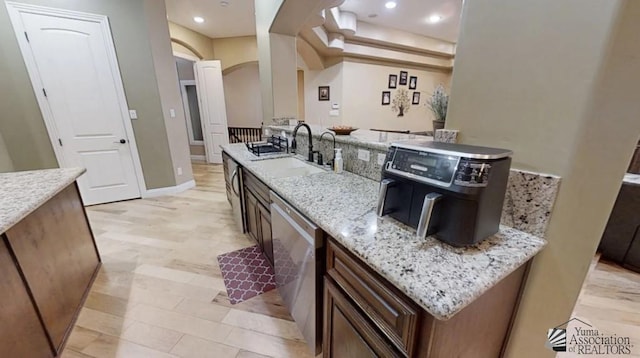 kitchen with light stone countertops, a sink, arched walkways, recessed lighting, and stainless steel dishwasher