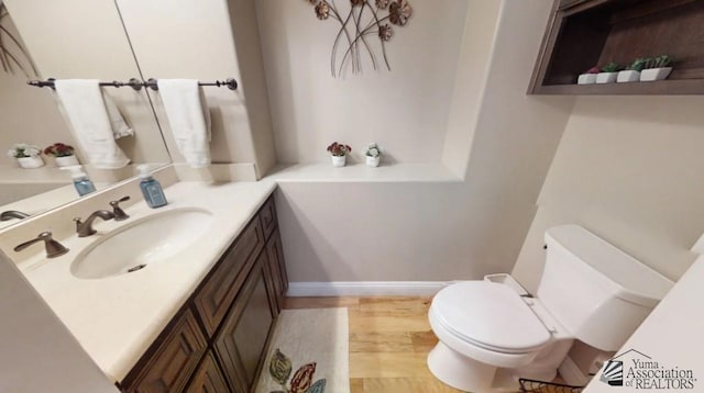 half bathroom with toilet, baseboards, wood finished floors, and vanity