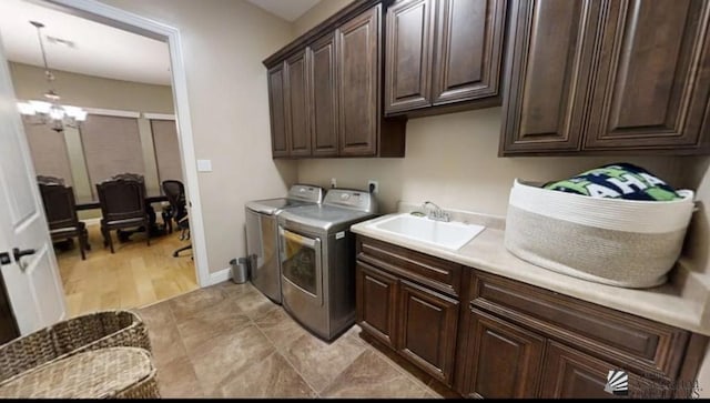 clothes washing area with a sink, cabinet space, a notable chandelier, and washer and clothes dryer