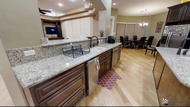 kitchen with light stone countertops, a sink, light wood finished floors, appliances with stainless steel finishes, and a notable chandelier