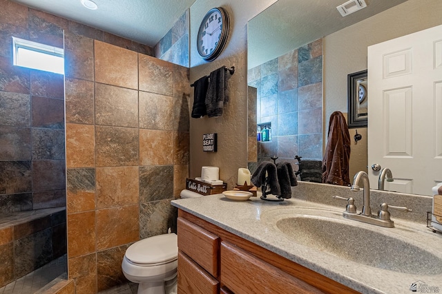 bathroom featuring a tile shower, vanity, and toilet