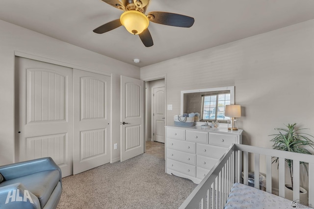 bedroom featuring a nursery area, a closet, light colored carpet, and ceiling fan