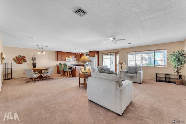 living room featuring light carpet, a textured ceiling, visible vents, and a ceiling fan