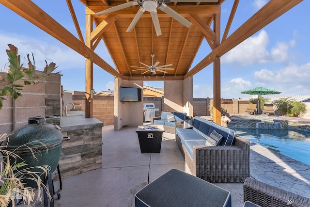 view of patio featuring a fenced in pool, ceiling fan, a grill, an outdoor living space with a fire pit, and an outdoor kitchen