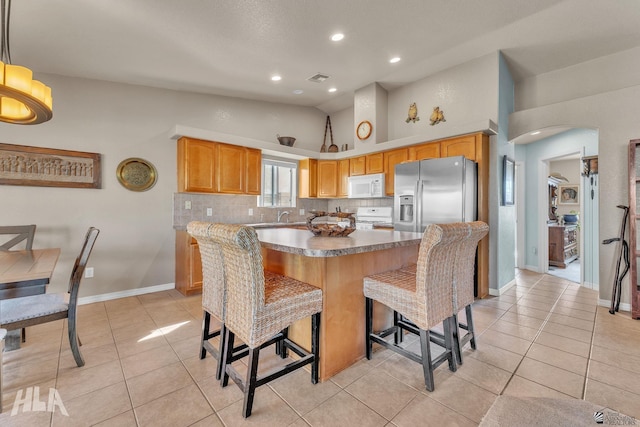 kitchen featuring tasteful backsplash, a kitchen bar, light tile patterned floors, and white appliances