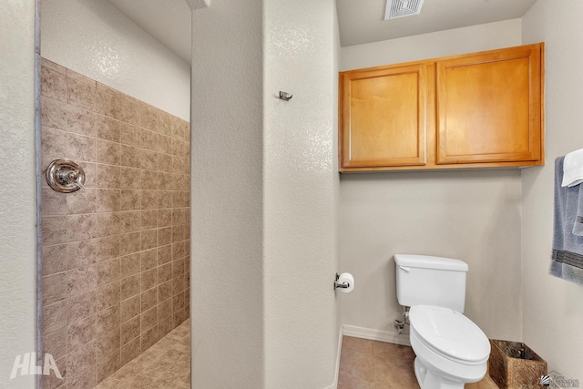 bathroom with tile patterned flooring, tiled shower, and toilet