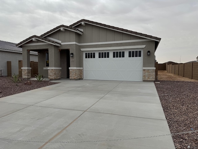 craftsman-style home featuring board and batten siding, fence, a garage, stone siding, and driveway