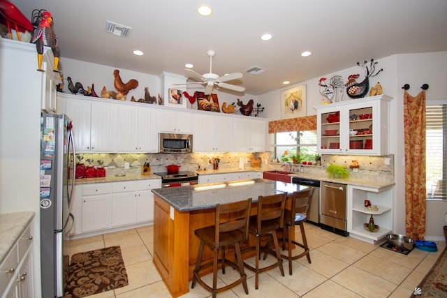 kitchen featuring stainless steel appliances, a kitchen island, light stone counters, light tile patterned flooring, and white cabinets