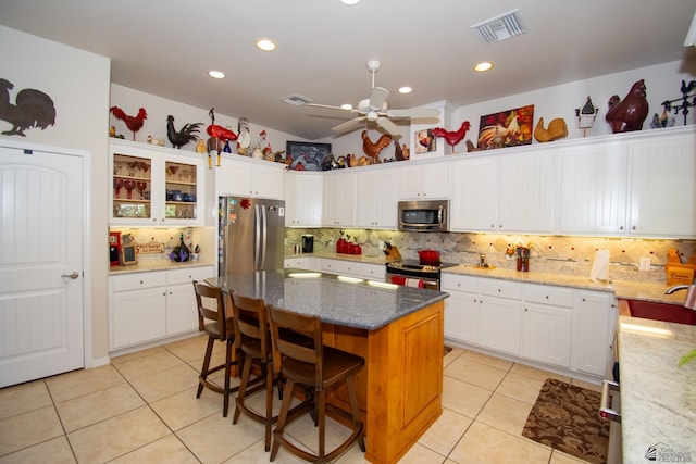 kitchen featuring light stone countertops, decorative backsplash, stainless steel appliances, white cabinets, and a center island