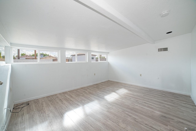 empty room featuring beam ceiling and light hardwood / wood-style flooring