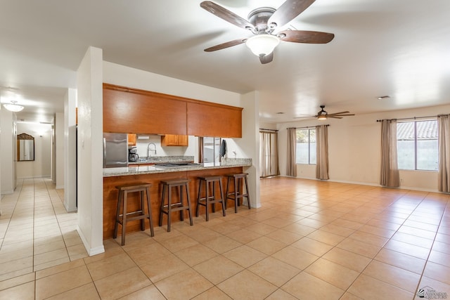 kitchen with stainless steel refrigerator, sink, a kitchen bar, light tile patterned floors, and kitchen peninsula