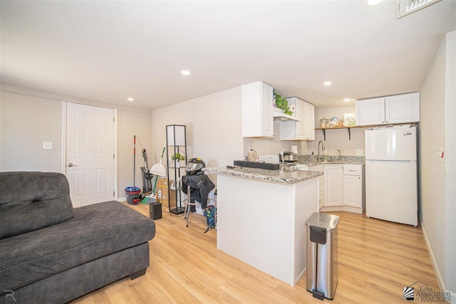 kitchen with white refrigerator, light hardwood / wood-style flooring, white cabinetry, and light stone counters