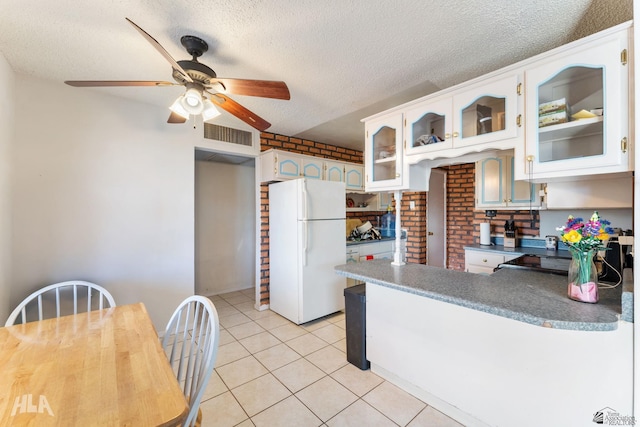 kitchen featuring a textured ceiling, light tile patterned floors, white cabinetry, white refrigerator, and ceiling fan