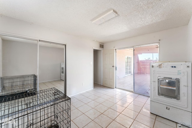 clothes washing area with washer / dryer, a textured ceiling, and light tile patterned flooring