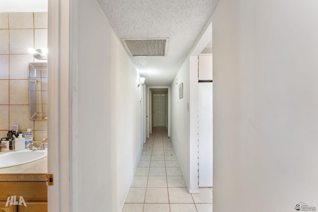 hallway featuring tile walls, a textured ceiling, light tile patterned floors, and sink