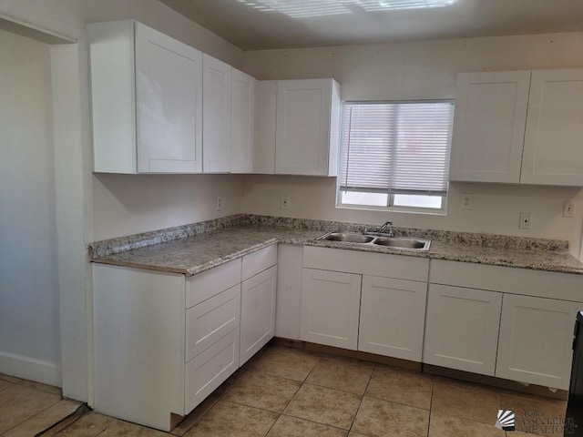 kitchen featuring light stone counters, white cabinetry, sink, and light tile patterned floors