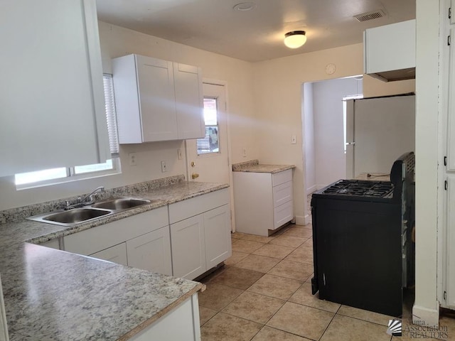 kitchen featuring black stove, sink, light tile patterned floors, white refrigerator, and white cabinets