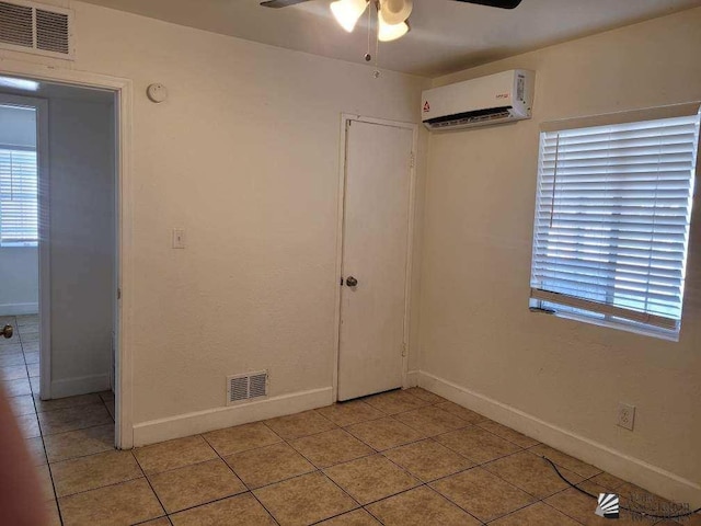 spare room featuring a wall unit AC, ceiling fan, and light tile patterned floors