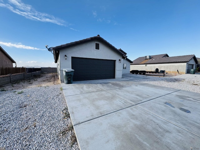 exterior space featuring stucco siding, driveway, a tile roof, fence, and a garage