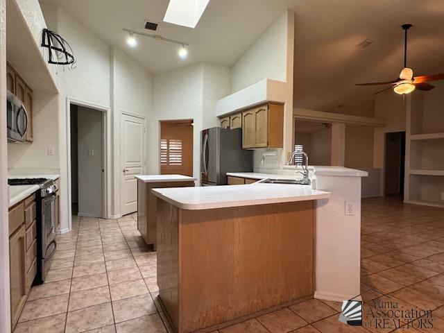 kitchen featuring sink, ceiling fan, appliances with stainless steel finishes, a skylight, and kitchen peninsula