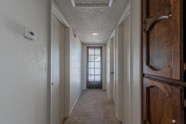 hall featuring a textured ceiling, carpet, and a textured wall