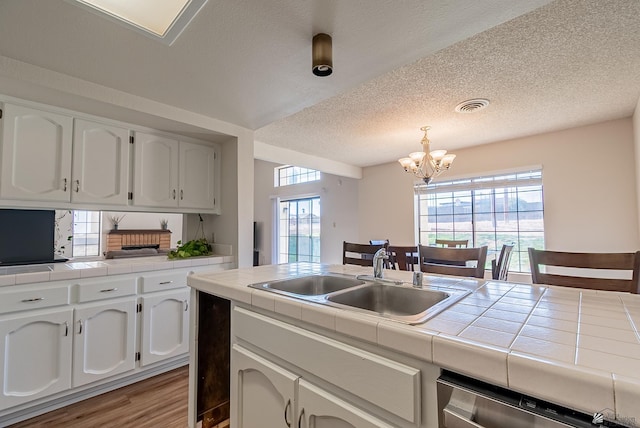 kitchen with tile counters, white cabinets, stainless steel dishwasher, and a sink