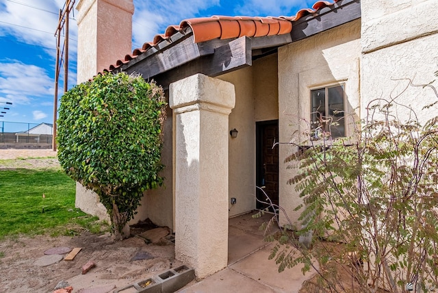 view of property exterior featuring a tile roof, fence, a chimney, and stucco siding