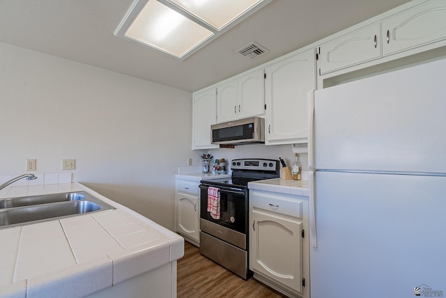 kitchen with visible vents, a sink, stainless steel appliances, tile counters, and white cabinetry