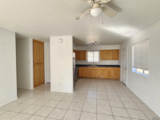 kitchen with light tile patterned floors, sink, a textured ceiling, ceiling fan, and stainless steel refrigerator