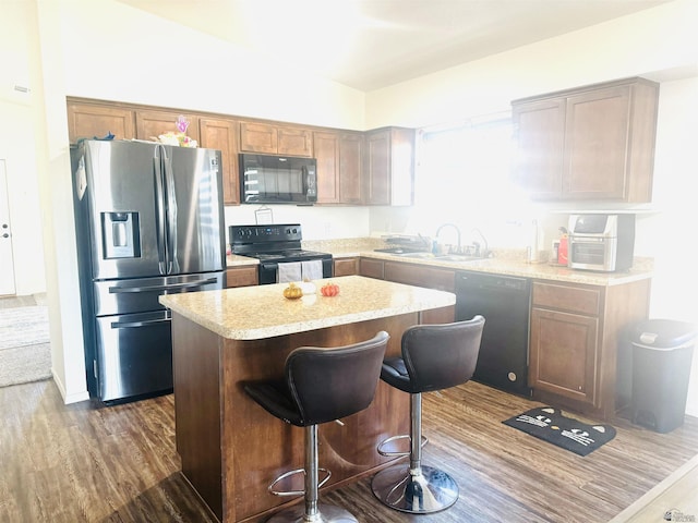 kitchen with a kitchen breakfast bar, dark hardwood / wood-style flooring, sink, black appliances, and a center island