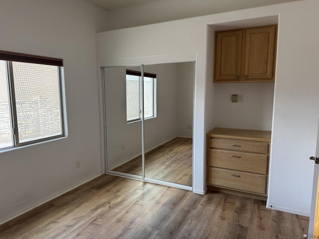 unfurnished bedroom featuring light wood-type flooring, baseboards, and a closet