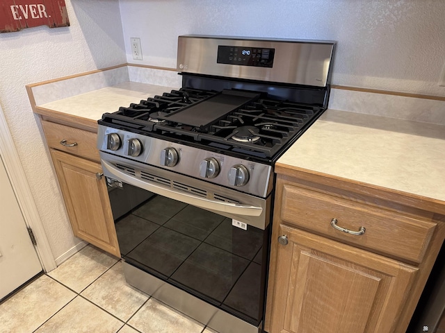 kitchen featuring a textured wall, stainless steel gas stove, light tile patterned flooring, and light countertops