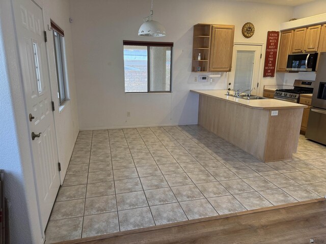 kitchen featuring open shelves, a peninsula, a sink, stainless steel appliances, and light countertops