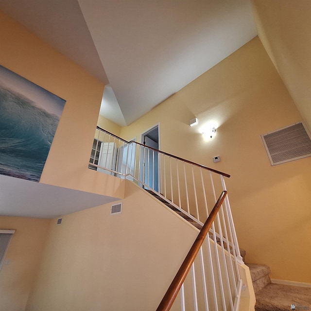 stairway with a towering ceiling, baseboards, visible vents, and carpet flooring