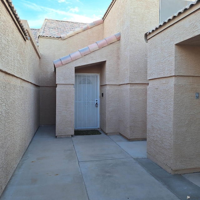 entrance to property with a patio area, stucco siding, and a tiled roof