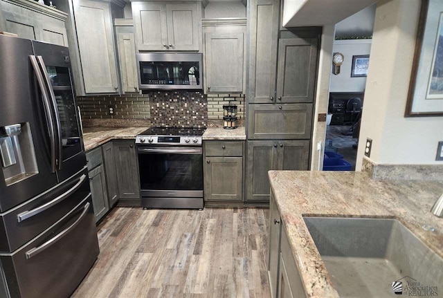 kitchen with decorative backsplash, gray cabinets, light stone countertops, and appliances with stainless steel finishes