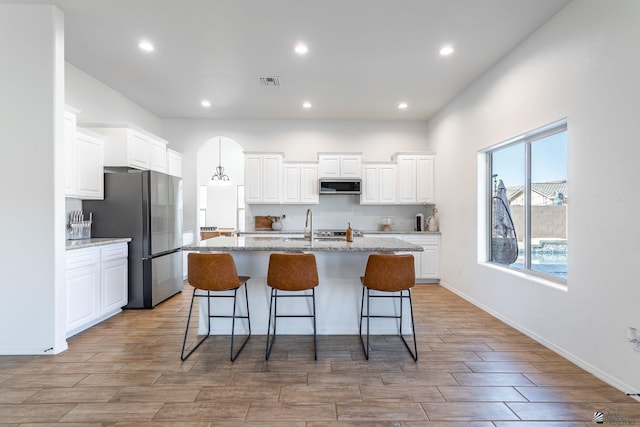 kitchen featuring a center island with sink, white cabinets, light stone countertops, and stainless steel appliances