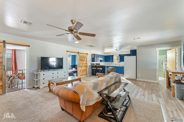 living room with ceiling fan, a barn door, and light hardwood / wood-style floors