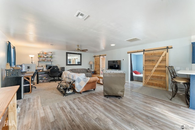 living room featuring light wood-type flooring, a barn door, and ceiling fan