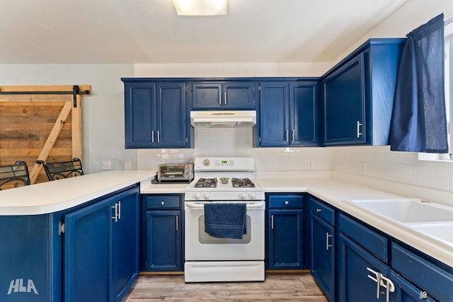 kitchen featuring a breakfast bar, a barn door, blue cabinets, and white gas range oven